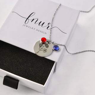 A silver floral disc pendant necklace with a red and blue gemstone accent, presented on a white jewelry box branded 'fnur'.