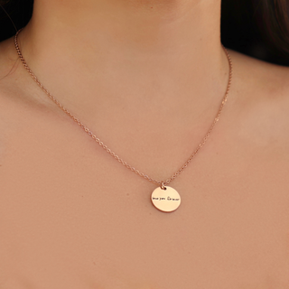 A close-up of a person's neck and chest wearing a delicate rose gold chain necklace with a small round engraved disc pendant that reads 'Love You Always'.