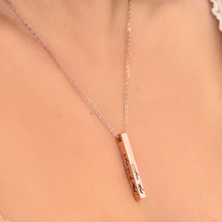 A close-up of a person's neck and upper chest wearing a delicate rose gold necklace with a vertical bar pendant engraved with 'I love you' in black script.