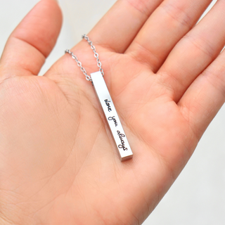 A silver bar necklace with the words 'love you always' engraved in black script, held in a person's open hand.