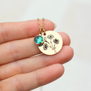 Gold necklace with a green gemstone and floral design held between fingers on a white background