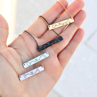 Close-up of rose gold, silver, black, and gold long-distance necklaces displayed on a hand, engraved with custom states and heart design, personalized jewelry gift.