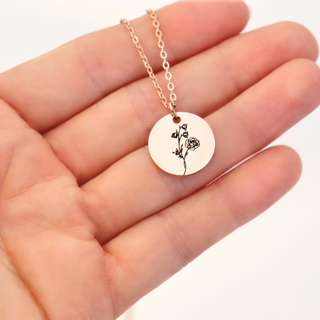 Necklace with a round pendant featuring a floral design held in a hand against a white background